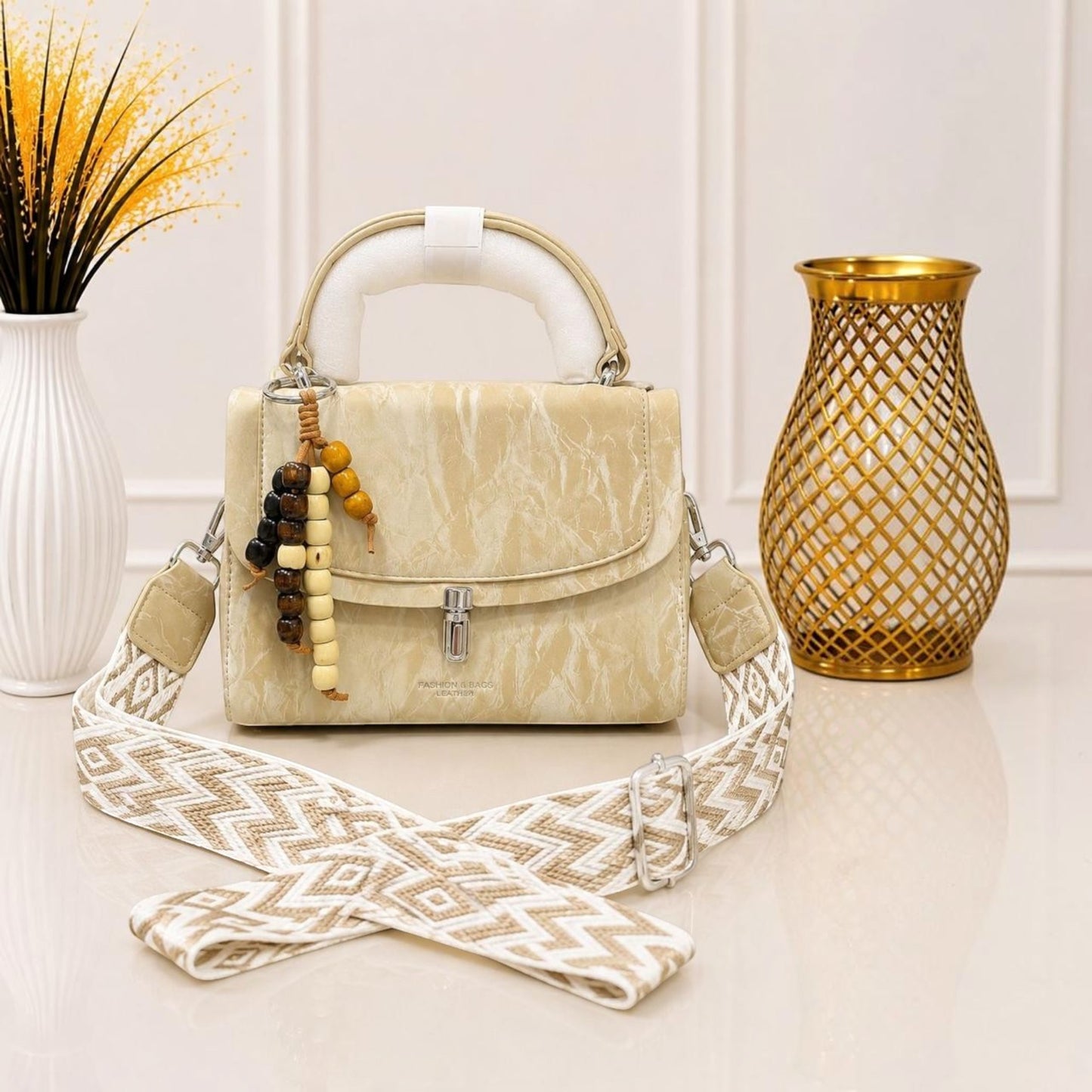 Evnique structured beige marble-effect top handle handbag with a beaded charm and woven guitar-style crossbody strap.