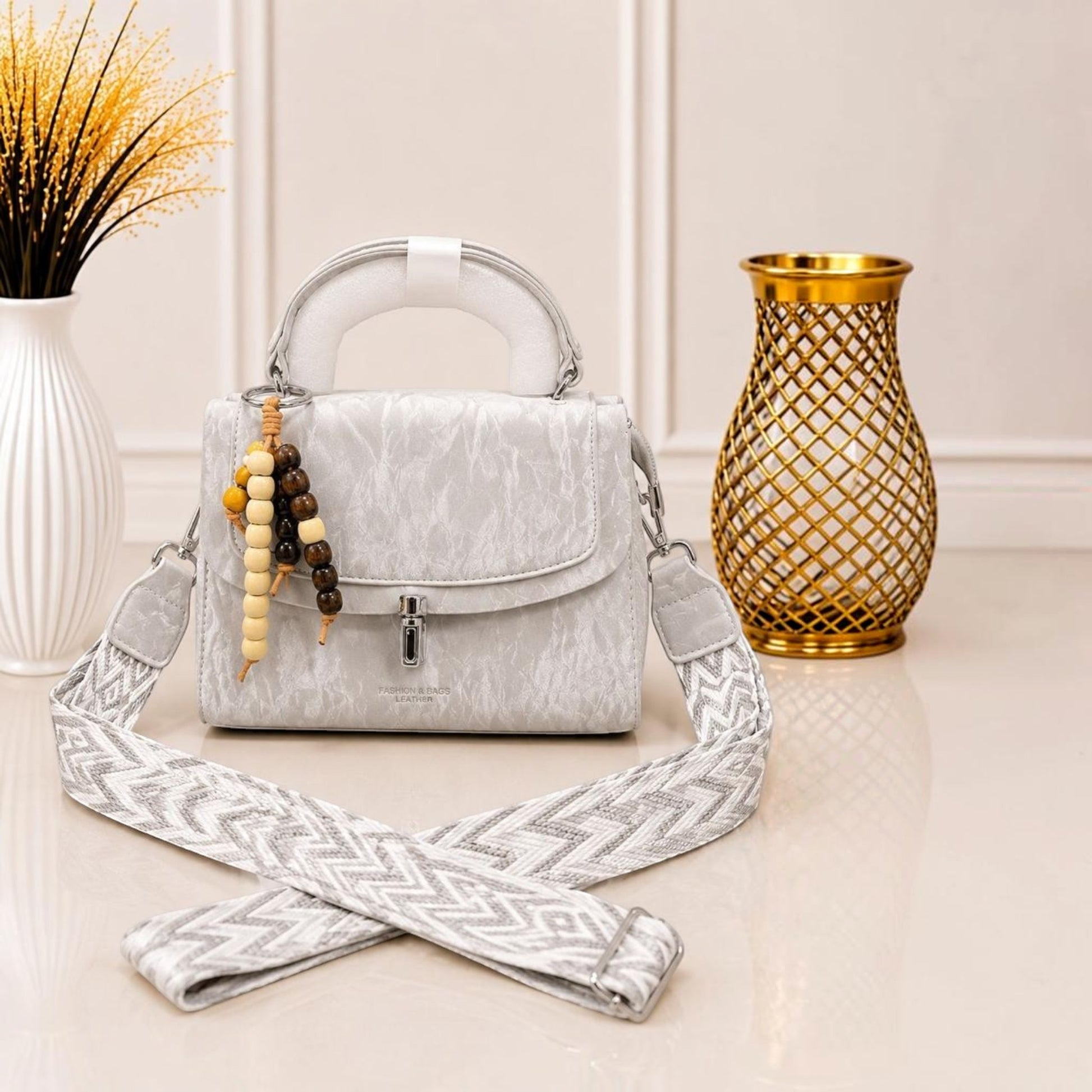 Evnique grey marble-effect structured top-handle handbag with a beaded charm and a wide woven guitar-style strap.